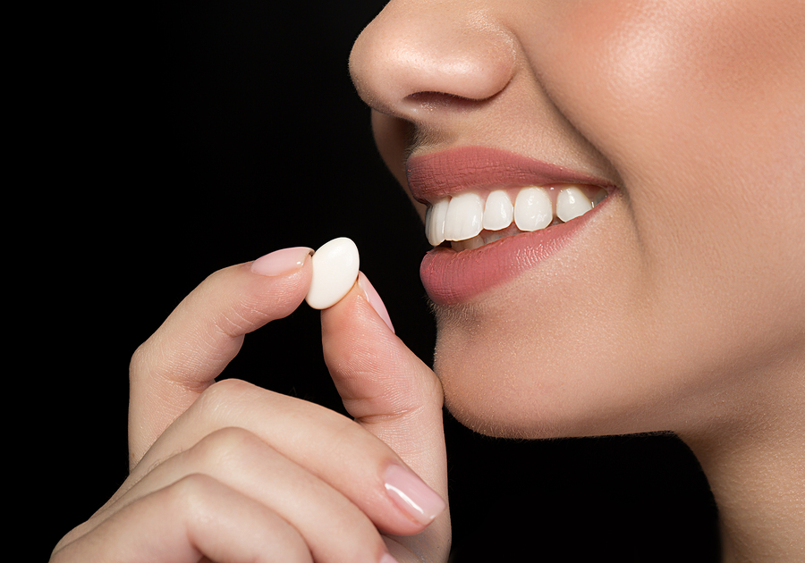 Close up side view of young positive woman is putting chewing gum into her mouth. Fresh breath concept. Isolated on dark background