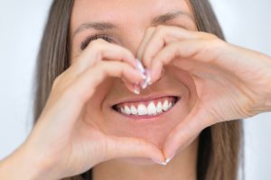 Teeth care. Dental care. Healthy teeth. Perfect white smile. Woman holding heart shaped hands near strong healthy teeth. Stomatology or dentistry concept