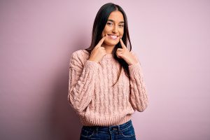 Young woman with long brown hair smiling. She's wearing a pick knit sweater and dark blue jeans.