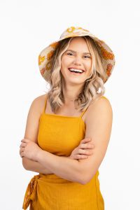 woman wearing a yellow sundress and hat smiling