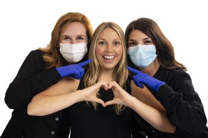 woman smiling and making a heart with her hands while standing between two dental hygienists